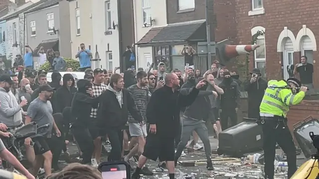 A group of men throw a traffic cone at a police officer