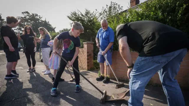 Sebastian Taylor sweeps the street with other volunteers