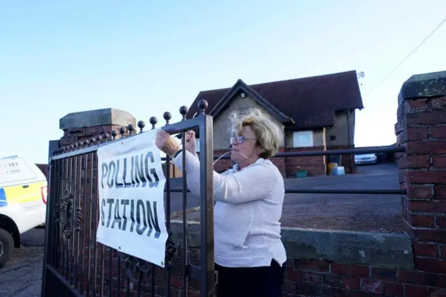 Woman putting up a Polling Station sign on a gate