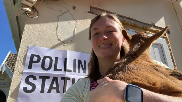 Nym the goat being held in front of a polling station sign