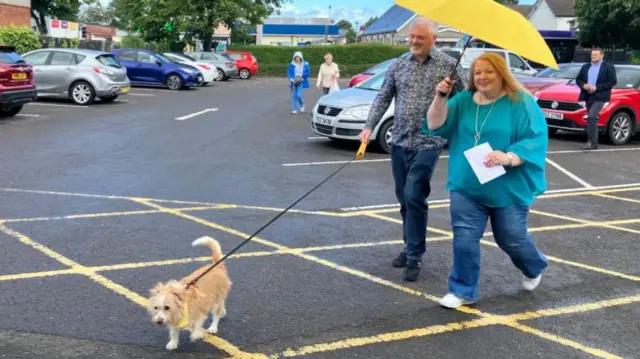 Alliance Party leader Naomi Long and her husband Michael Long with their dog Daisy walking through a carpark