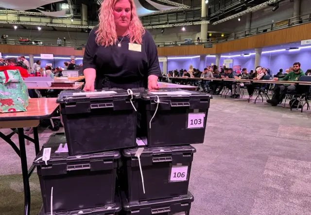 A woman with blond hair and black boxes ready to count