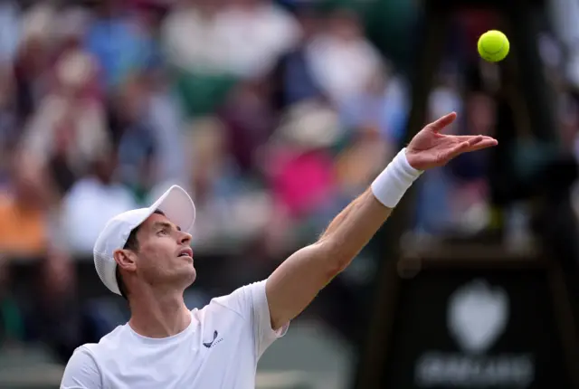 Andy Murray throws the ball to serve in a white t-shirt and white cap