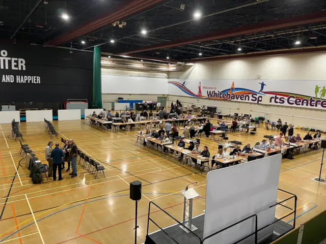 People sitting at tables in a large sports hall