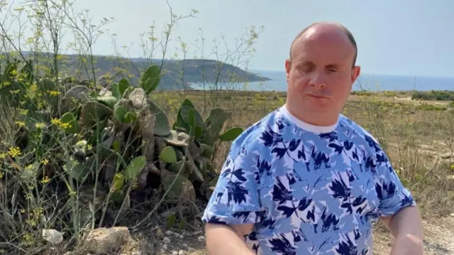 Paul wears a blue and white graphic T-shirt in front of cacti