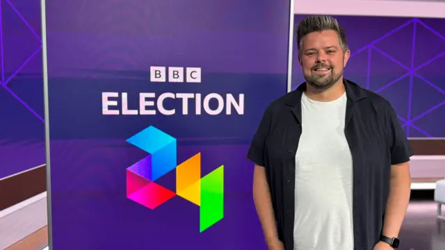 BBC presenter Adam Crowther stands in front of a screen displaying the BBC Election '24 logo.