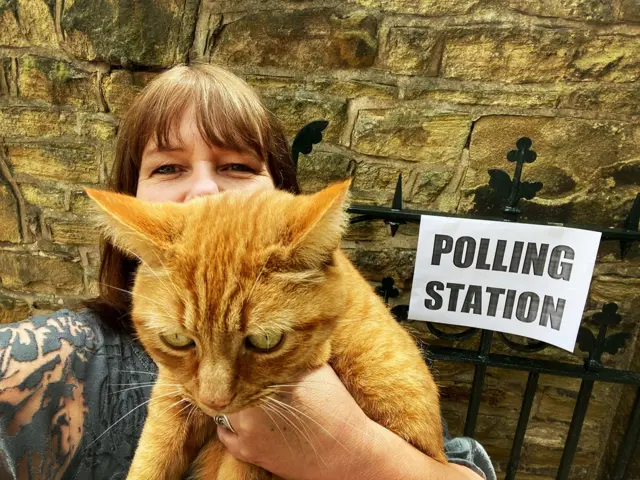 Woman holding her cat to the camera with a polling station sign in the background