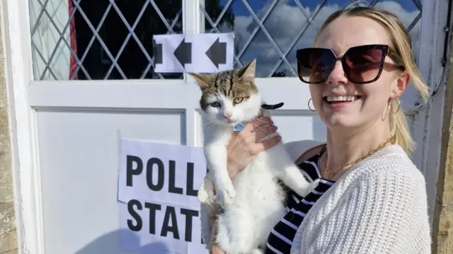 Tuti the cat being held by Rowena Jones outside a polling station sign