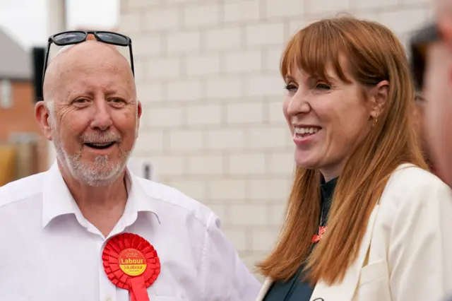 A man with a white beard talks to a woman with red hair