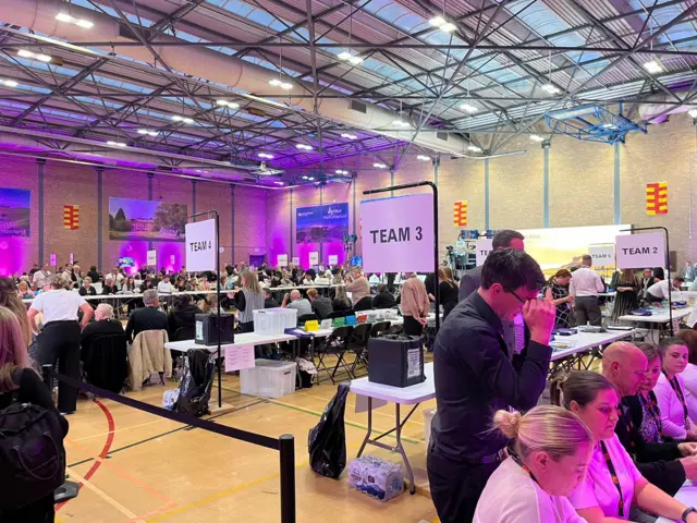 People sit at tables in a sports hall