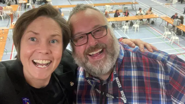 Kelly Morgan and Carl Humphries from BBC Radio Wiltshire taking a selfie over the leisure centre banister with the count behind