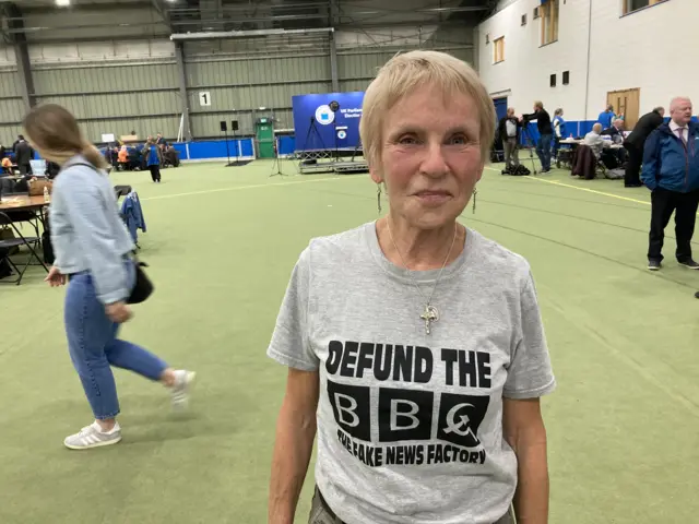 Anne McCloskey at the count centre wearing a grey t-shirt with 'defund the BBC' written on it