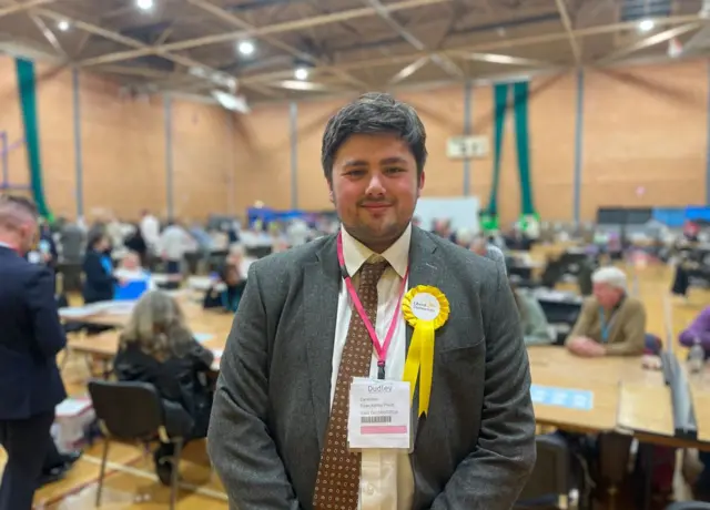 A man with a suit and a yellow rosette