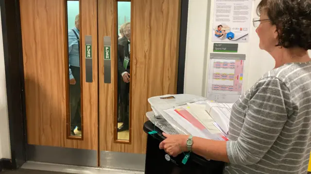 Woman holding ballot box standing in front of a door