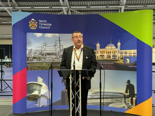 A man stands at a lectern on a stage