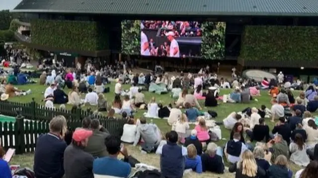 Fans watching a tennis match on a large screen