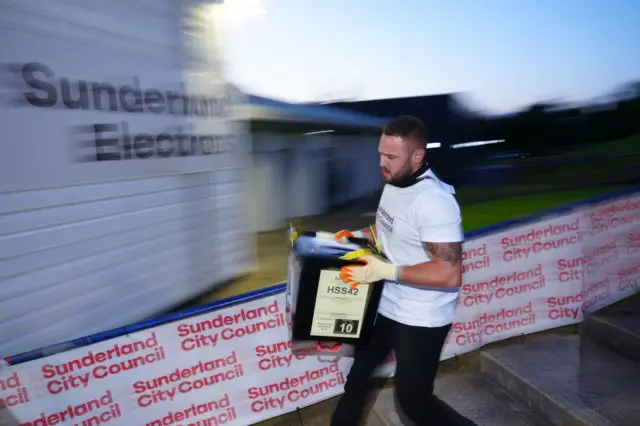 A man in a white shirt carries a large black box