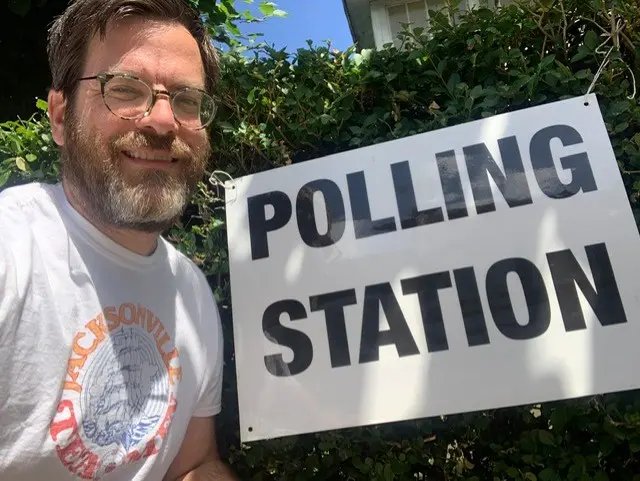 A man with a beard next to a polling station sign