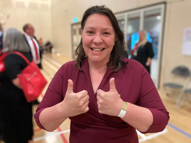 A woman holds her thumbs up to the camera