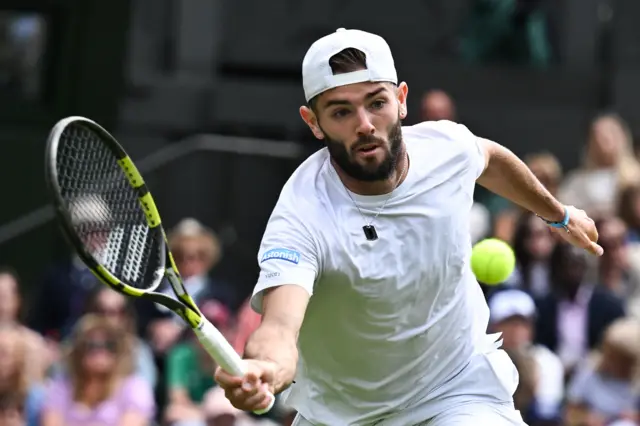 Jacob Fearnley hits a forehand volley wearing a white shirt with a white cap