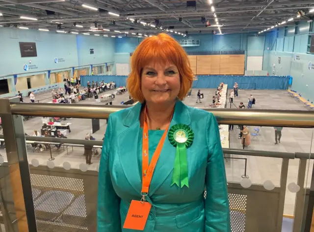 A lady in a green suit and orange hair smiling