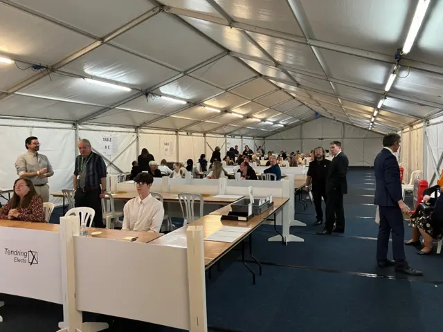 People sitting and standing inside a marquee at the Harwich and North Essex count in Clacton