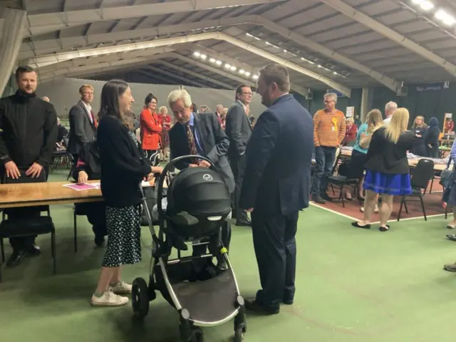 Alex McIntyre with his baby and wife, with Richard Graham looking into a pram.