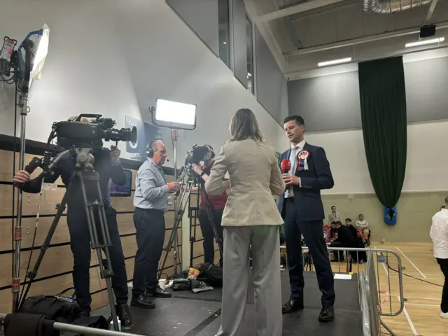 man being interviewed by reporter in front of cameras