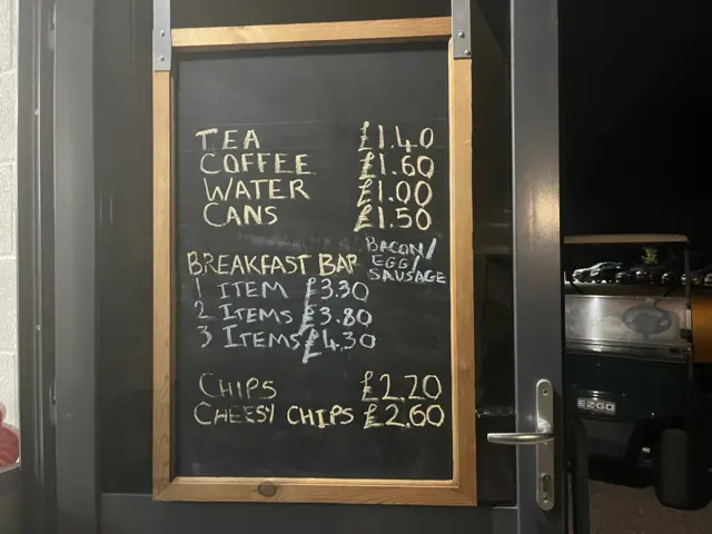 A blackboard with the price of refreshments on at the Forest of Dean count, including tea for £1.40, a three item breakfast bap for £4.30, and chips with cheese for £2.60