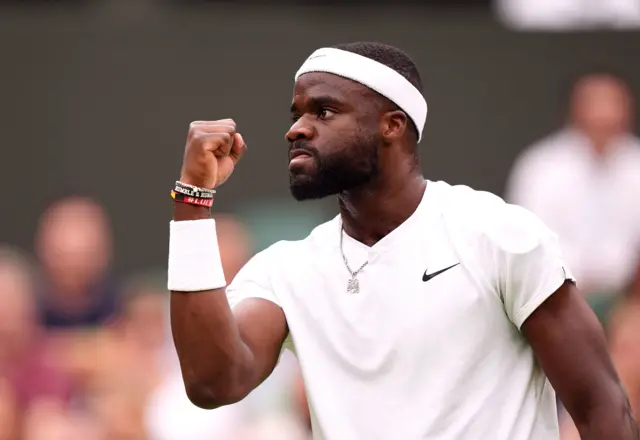 Frances Tiafoe clenches his fist in celebration wearing an all-white Nike top and white Nike headband