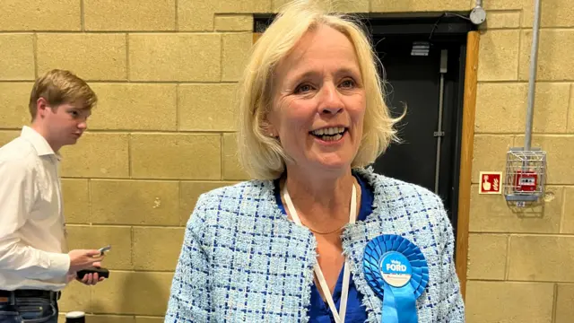 Vicky Ford wears a blue plaid jacket and blue rosette