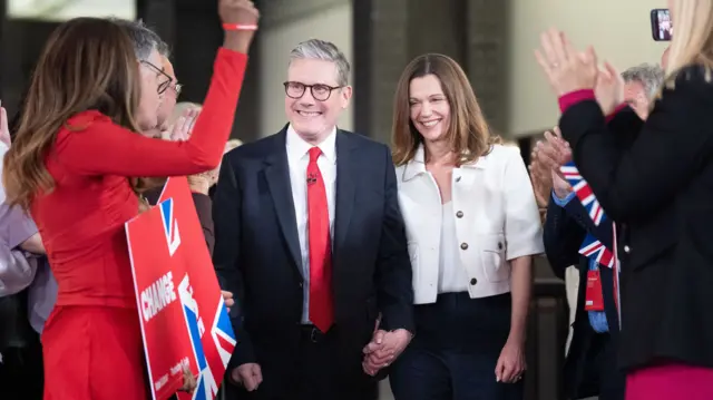 Starmer and his wife Vic hold hands as people cheer around them