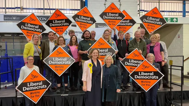 Anna Sabine and Tessa Munt posing in front of people holding Liberal Democrats banners