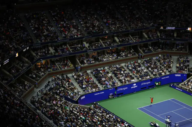 Wide shot of a corner of the Arthur Ashe Stadium at the US Open as the crowd watches Frances Tiafoe serve