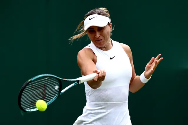 Paula Badosa hits a forehand shot wearing an all-white Nike dress and white visor cap