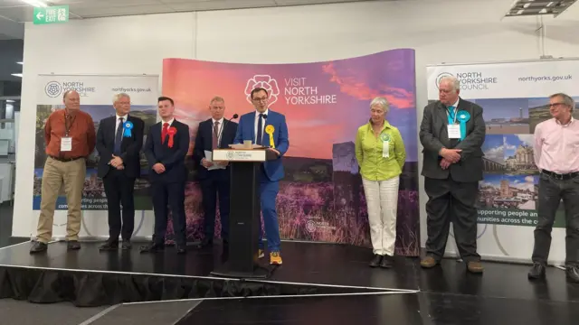 Tom Gordon stands at a lectern alongside other candidates