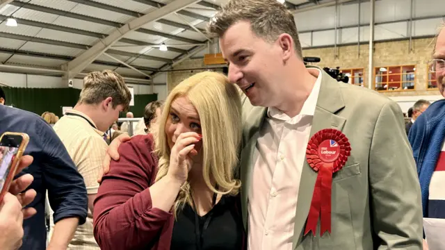 Mike Reader with short brown hair, brown jacket and red rosette