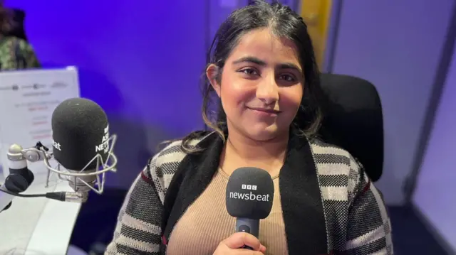 Woman holding a BBC microphone while seated in a studio