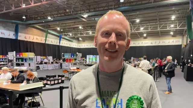 Paul Mannion with short fair hair wearing a green rosette at a count