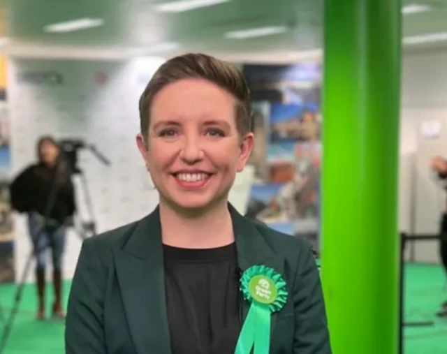 Carla Denyer smiling wearing green suit.