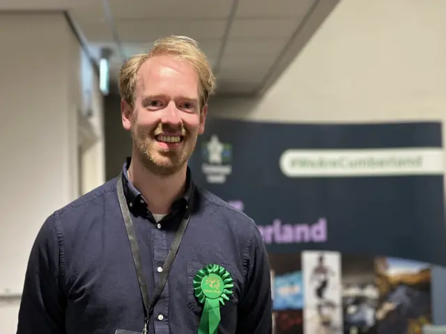 Green party candidate Gavin Hawkton wearing a blue shirt and a green rosette