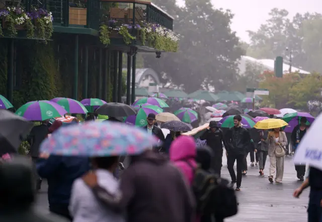 Crowds walking around Wimbledon holding umbrellas in the rain