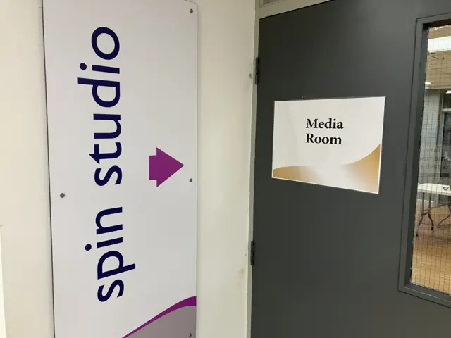 A sign reading "Spin studio" with an arrow point at the door that has a sign reading "Media Room" stuck on it.