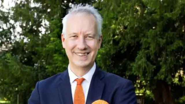 Gideon Amos head and shoulders shot wearing a suit and a liberal democrat rosette