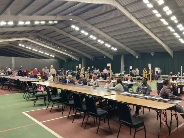 Vote counters talking and going on their phones at the count in a leisure centre