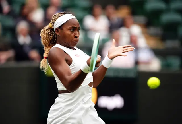 Coco Gauff hits a forehands shot wearing an all-white dress with white headband