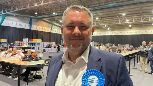 Jason Smithers with short grey hair and beard wearing a blue rosette at a count