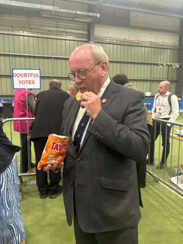 Jim Allister eating a bag of crisps