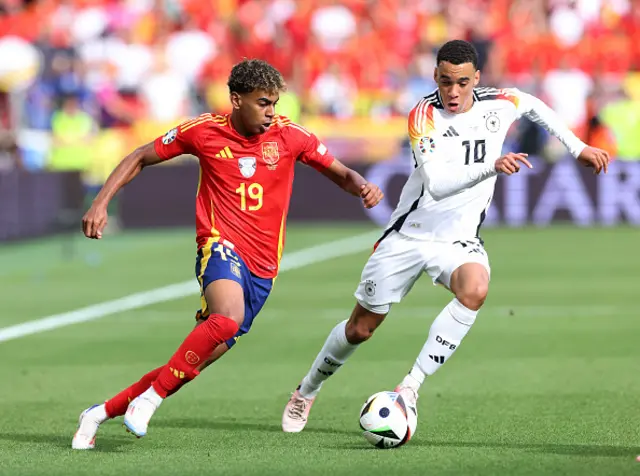 Lamine Yamal of Spain runs with the ball under pressure from Jamal Musiala