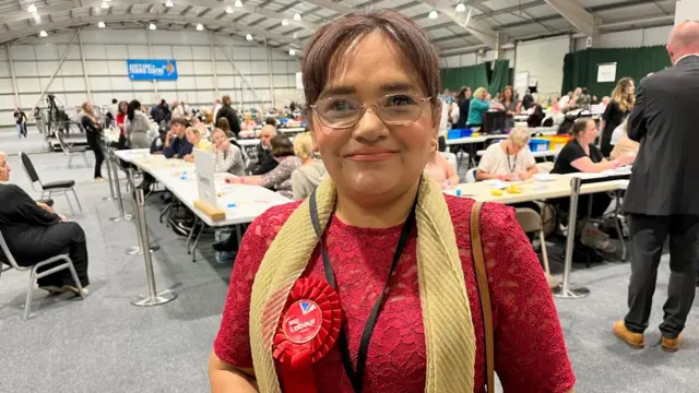 Rufia Ashraf with short dark hair wearing a red top and rosette at a count